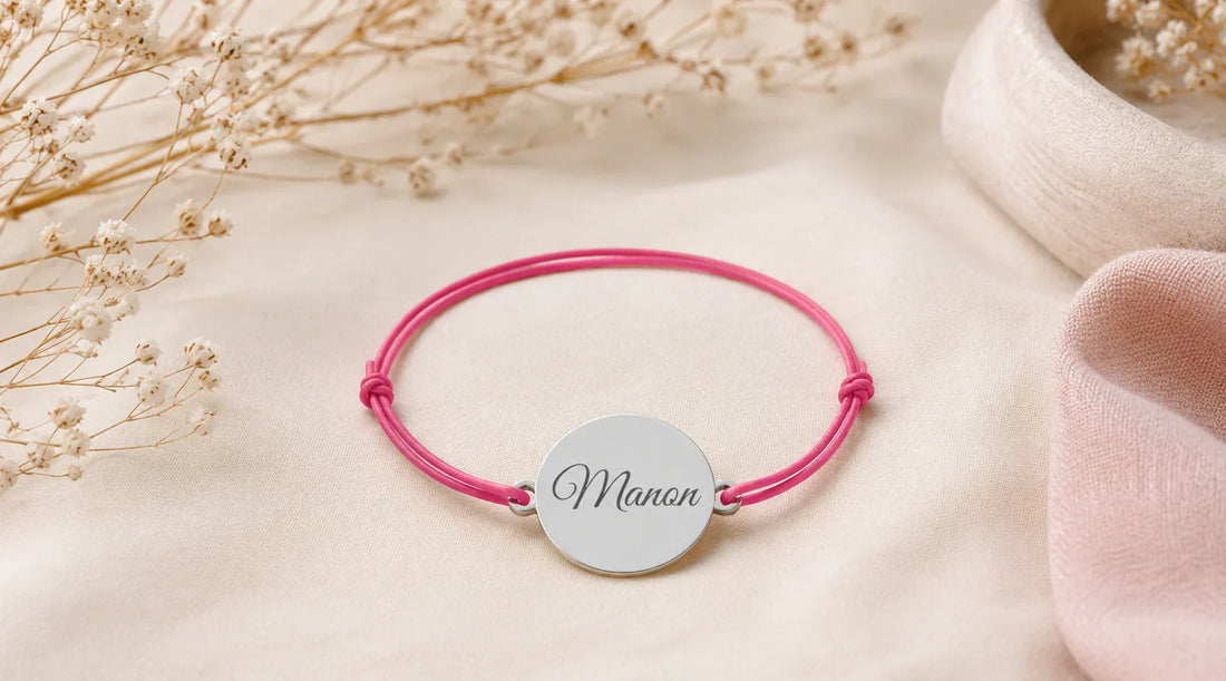 Bracelet cordon personnalisé avec médaille en argent gravée d’un prénom, présenté sur un tissu beige dans une ambiance élégante.