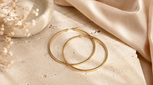 Boucles d'oreilles créoles Créolia doré en acier inoxydable sur fond beige élégant, style minimaliste Les Inséparables.