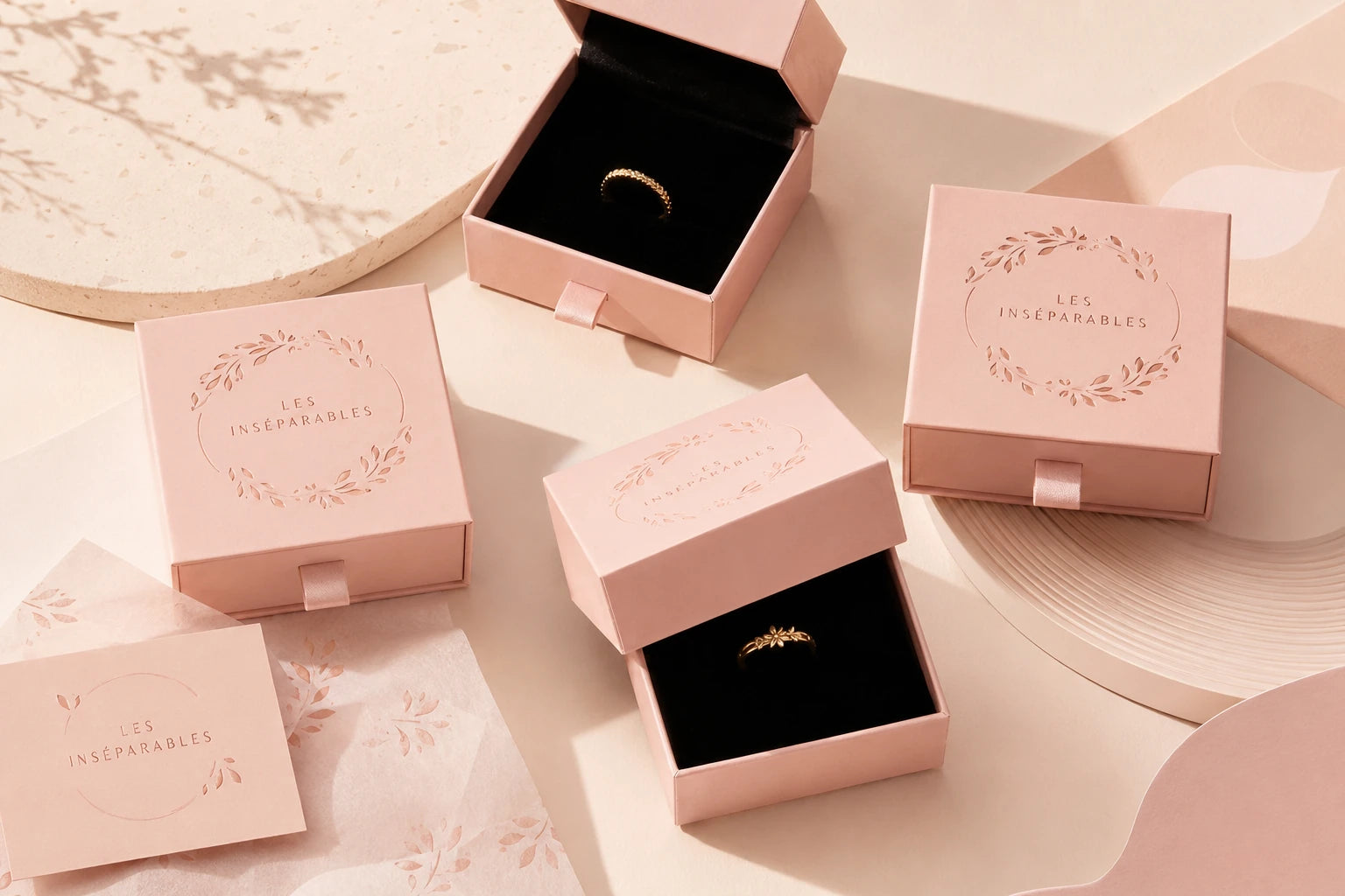 Boîtes à bijoux roses Les Inséparables, ouvertes et fermées, présentant des bagues dorées sur un décor beige et rose poudré.