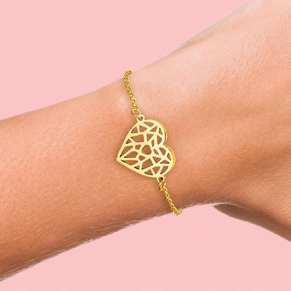 Bracelet chaîne Glamia doré en acier inoxydable avec pendentif cœur ajouré porté au poignet.