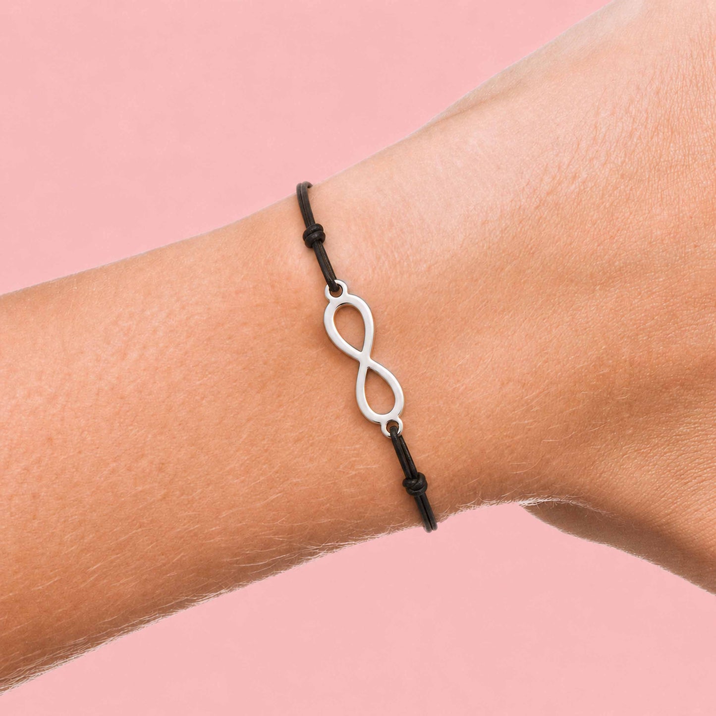 Bracelet fin en cordon noir avec symbole infini argenté porté au poignet sur fond rose pas