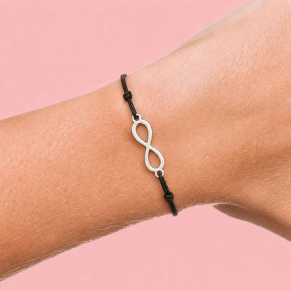 Bracelet fin en cordon noir avec symbole infini argenté porté au poignet sur fond rose pas