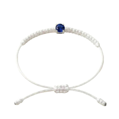 Bracelet cordon écru, pierre de saphir bleu de laboratoire sertie sur or 750/1000,
fermoir coulissant réglable
