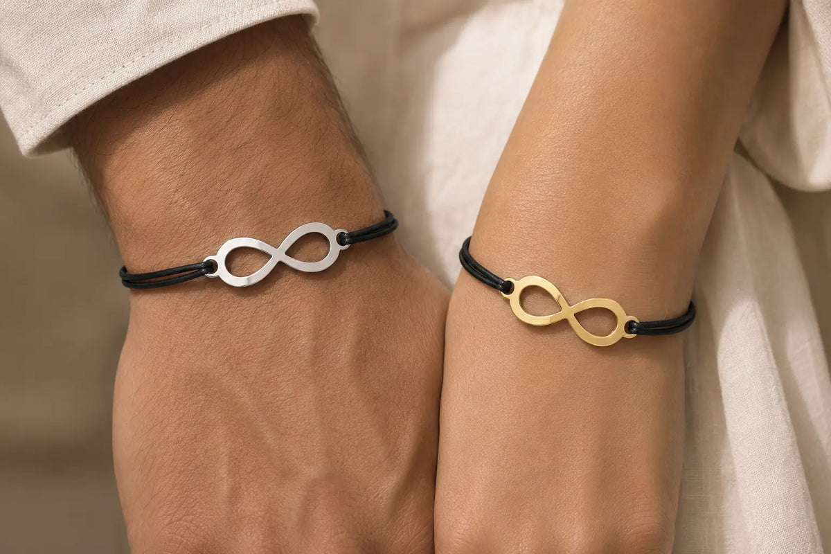 Couple portant des bracelets assortis avec symbole infini, l’un argenté et l’autre doré, montés sur un cordon noir.