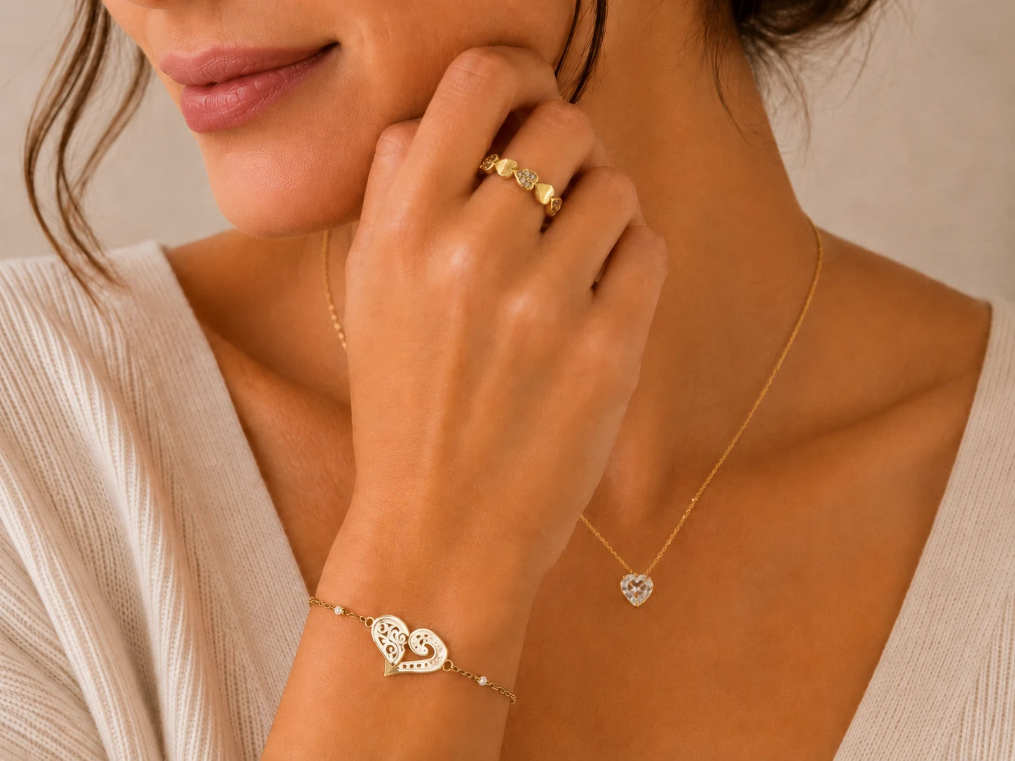 Femme portant un collier doré avec pendentif cœur, un bracelet cœur ajouré et une bague dorée ornée de petits cœurs.