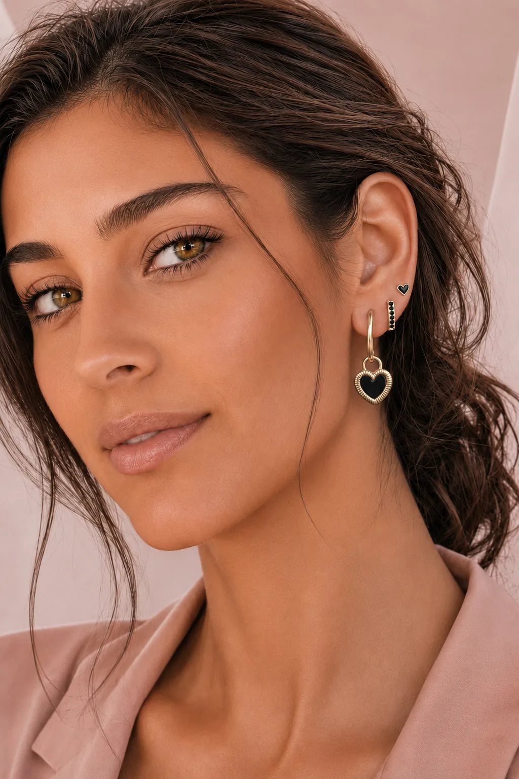 Femme portant une accumulation de boucles d’oreilles dorées et noires, avec une créole à pendentif cœur noir.
