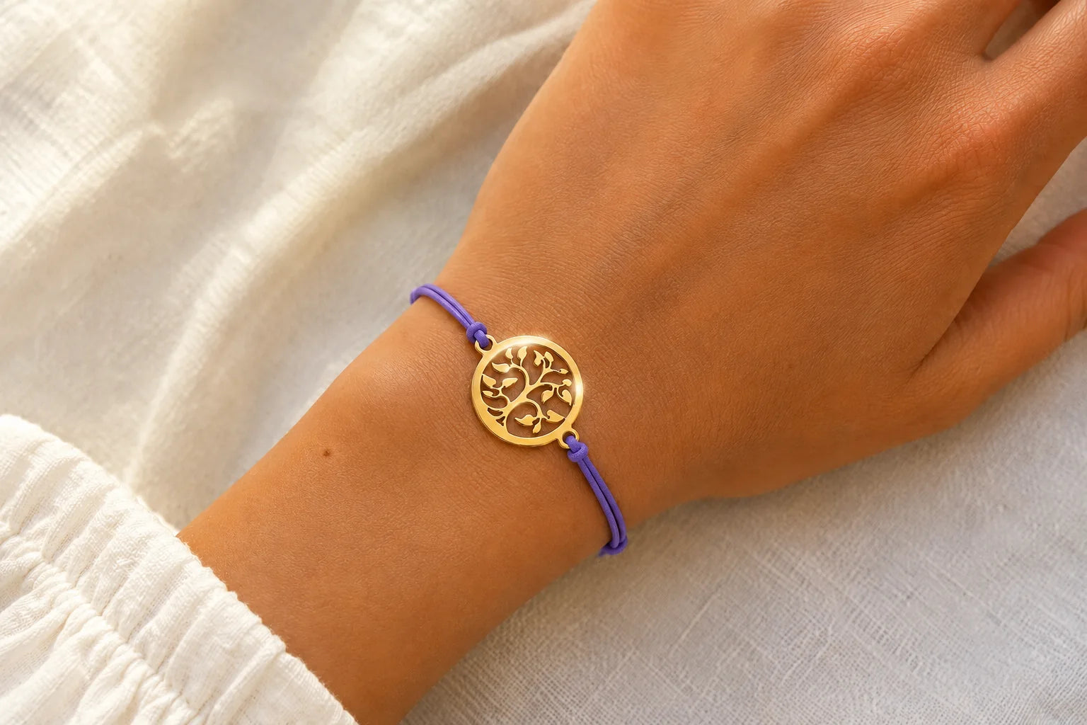 Femme portant un bracelet cordon violet avec un médaillon doré en forme d’arbre de vie.
