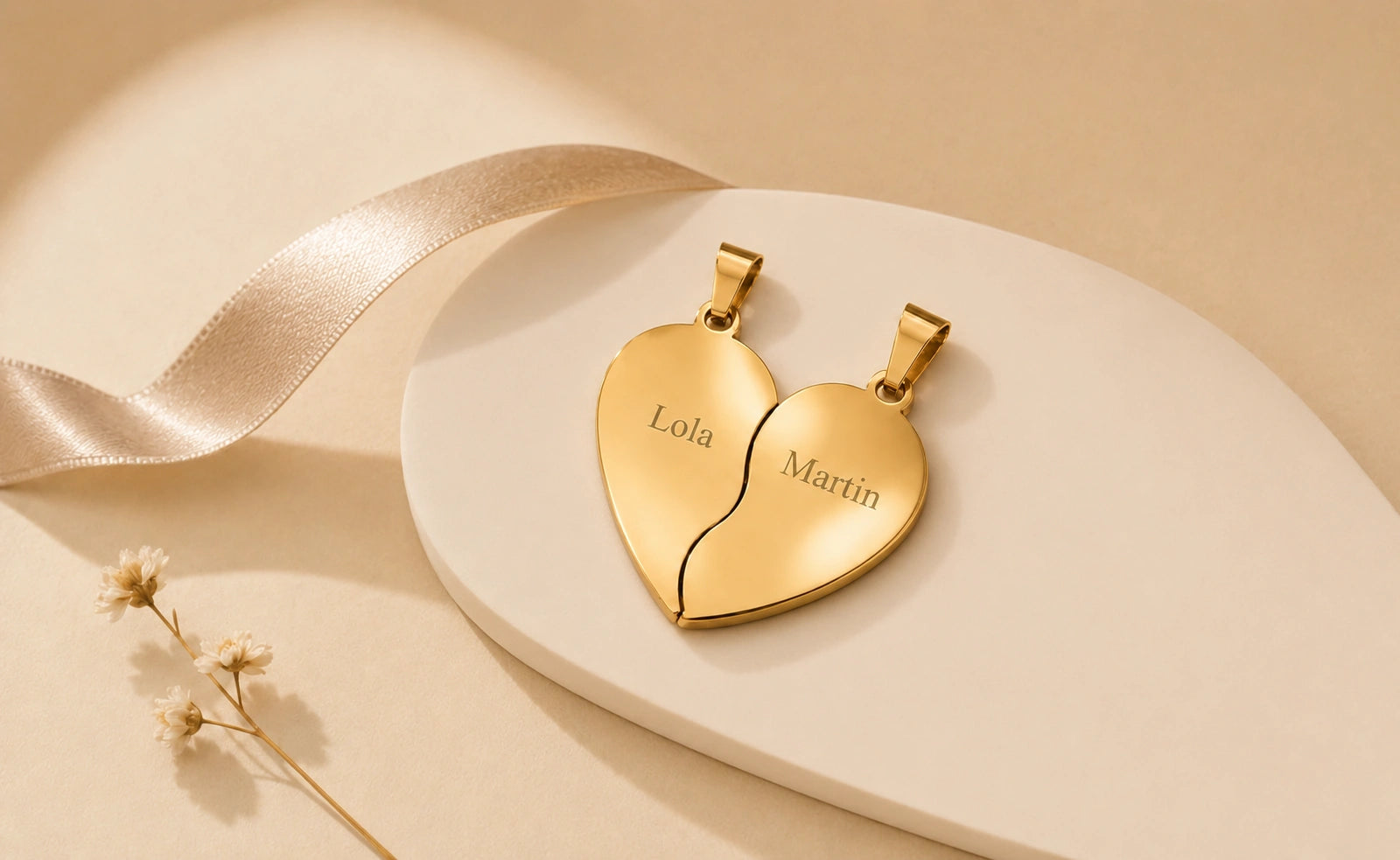 Pendentif cœur séparable doré personnalisé avec les prénoms Lola et Martin, présenté sur un support beige.