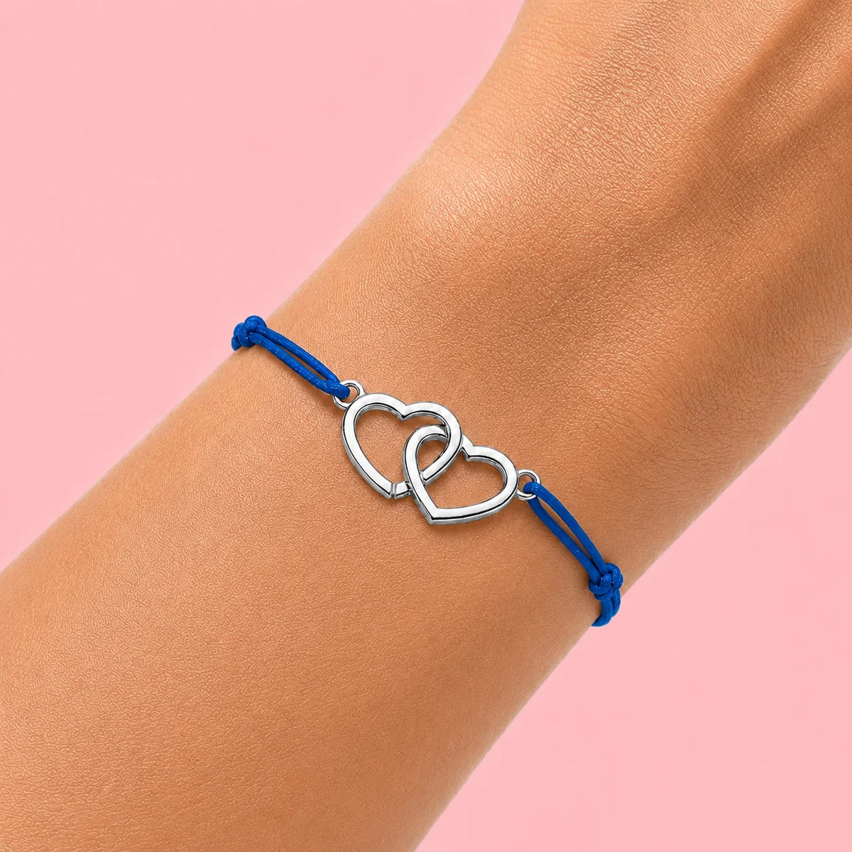 photo d'un poignet de femme qui porte un bracelet cordon bleu et coeurs entrecroisés en acier argenté 