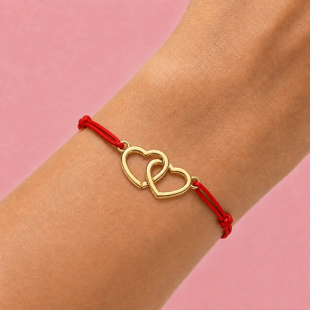 poignet qui porte un cordon rouge en bracelet vec coeurs entrecroisés en acier doré