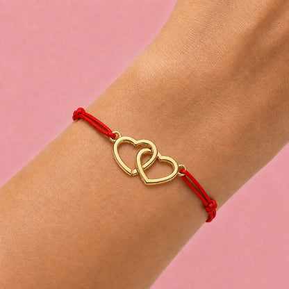 poignet qui porte un cordon rouge en bracelet vec coeurs entrecroisés en acier doré