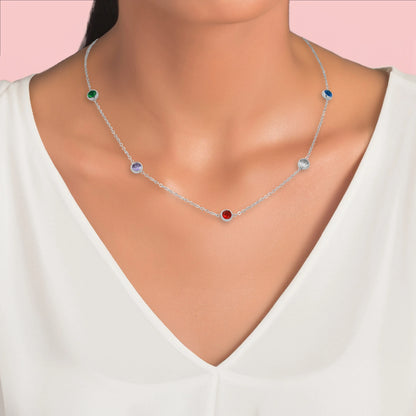 Collier chaîne argentée avec cinq pierres colorées, porté autour du cou d’une femme.